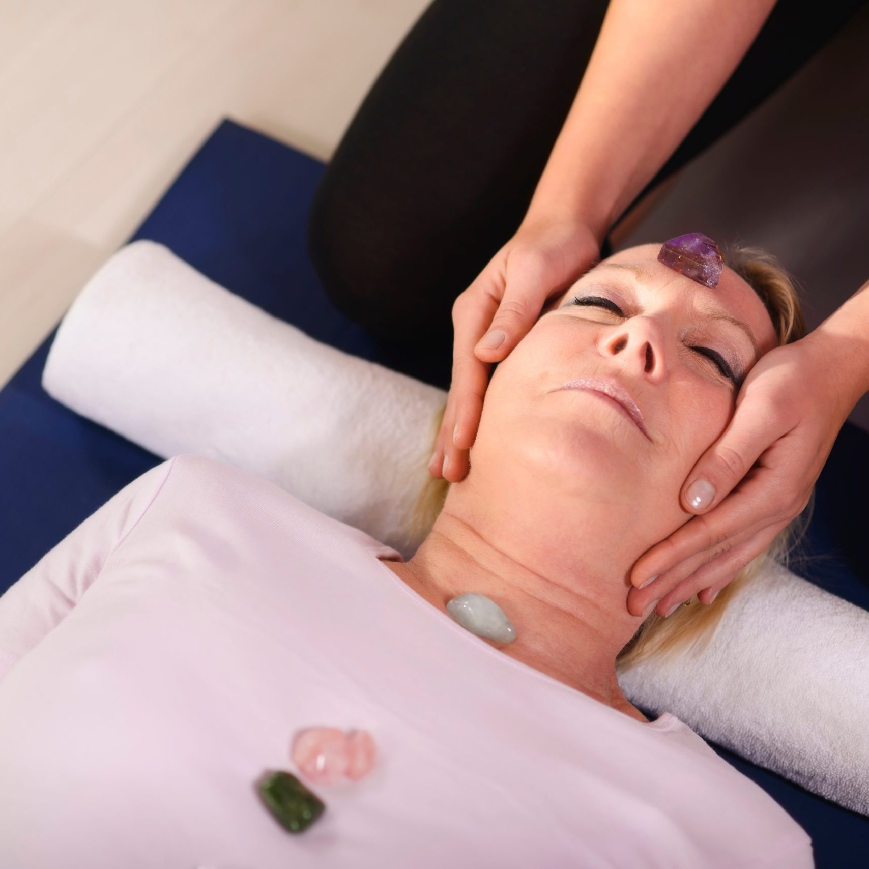 Reiki therapy with girl working as spirit healer, arranging crystals and gemstones on female client for treatment